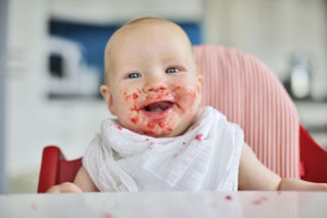 Baby nach dem Essen mit verschmiertem Mund am Tisch Baby nach dem Essen mit verschmiertem Mund am Tisch