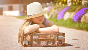 Mädchen lehnt auf Koffer vor der Familienreise